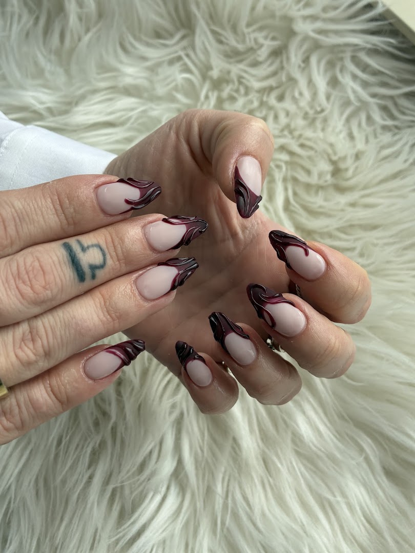 Dark burgundy flame French tip nails on long stiletto nails displayed on white fur